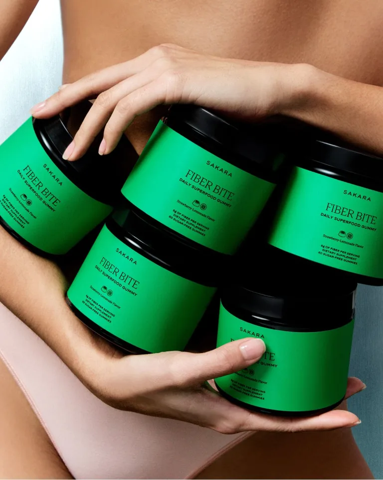 A woman holding 5 jars of Sakara Fiber bite